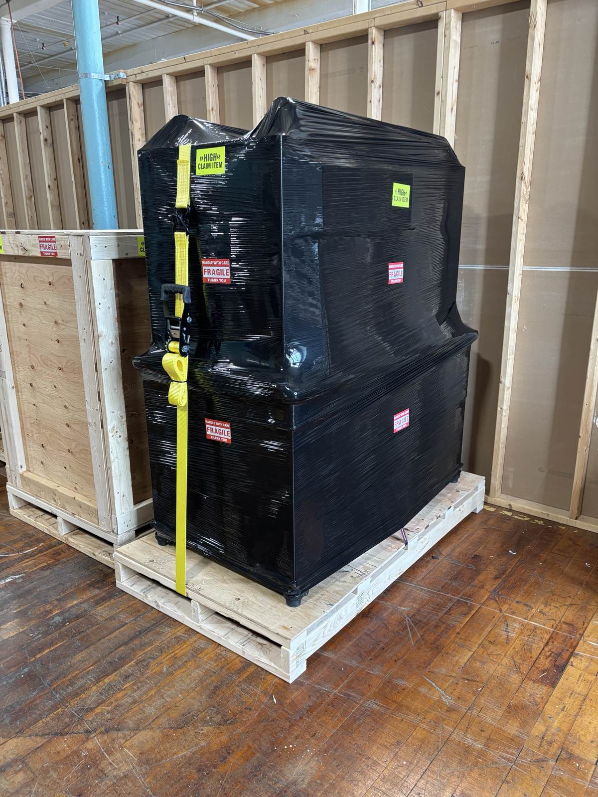 A tall, shrink-wrapped item strapped and marked as a high-claim shipment.